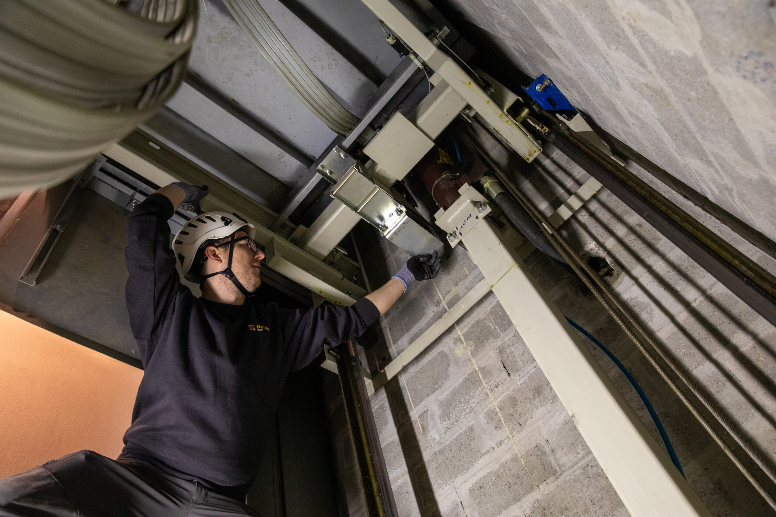 Inspecteur controleert technische onderdelen van een personenlift in de liftschacht

