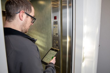 Liftkeuring na modernisatie in een professioneel gebouw door een controleur met tablet Contrôle d’un ascenseur après modernisation dans un bâtiment professionnel, réalisé par un inspecteur à l’aide d’une tablette